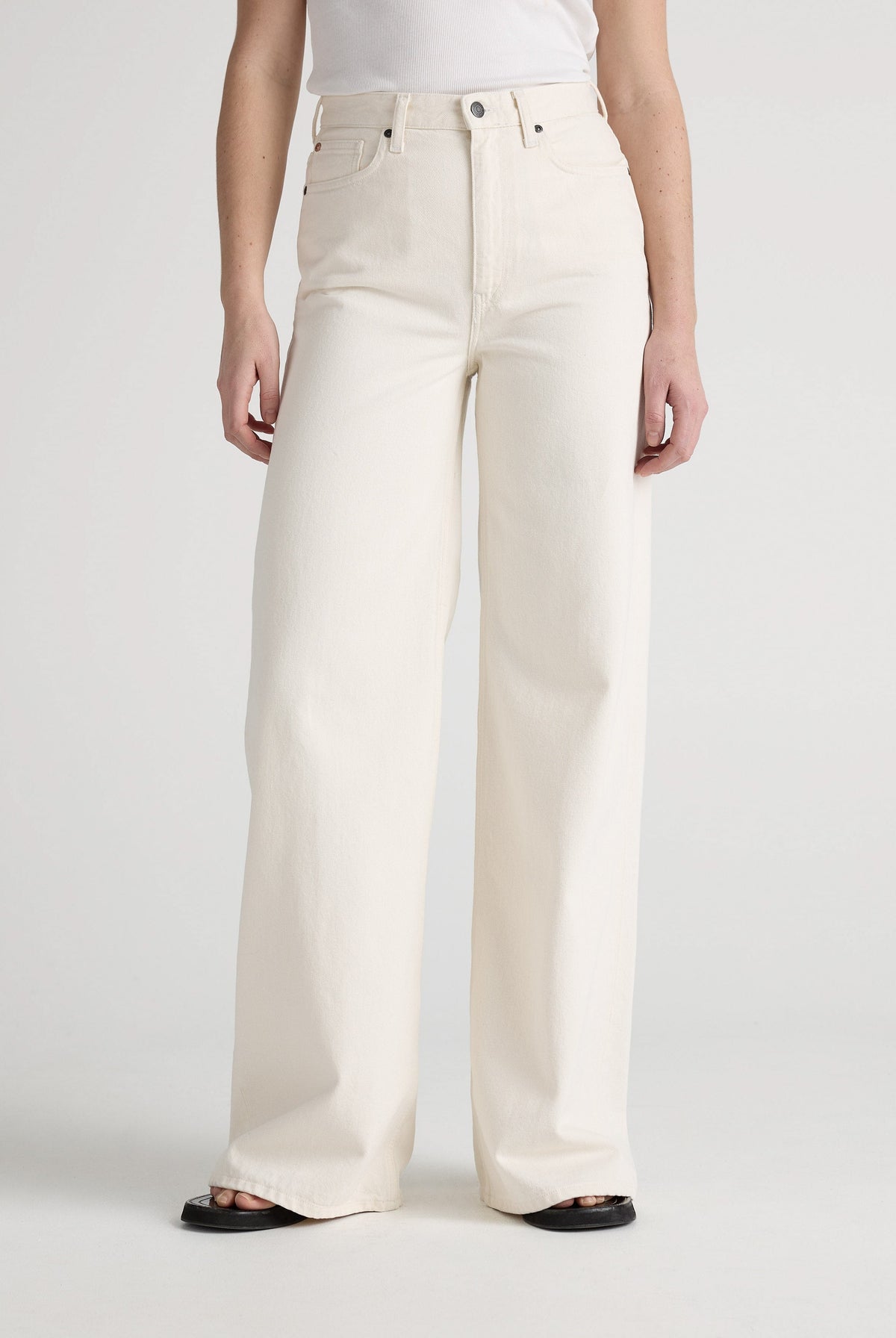 Wide-leg cream jeans in organic cotton, displaying high-waisted design paired with a simple white tank top.