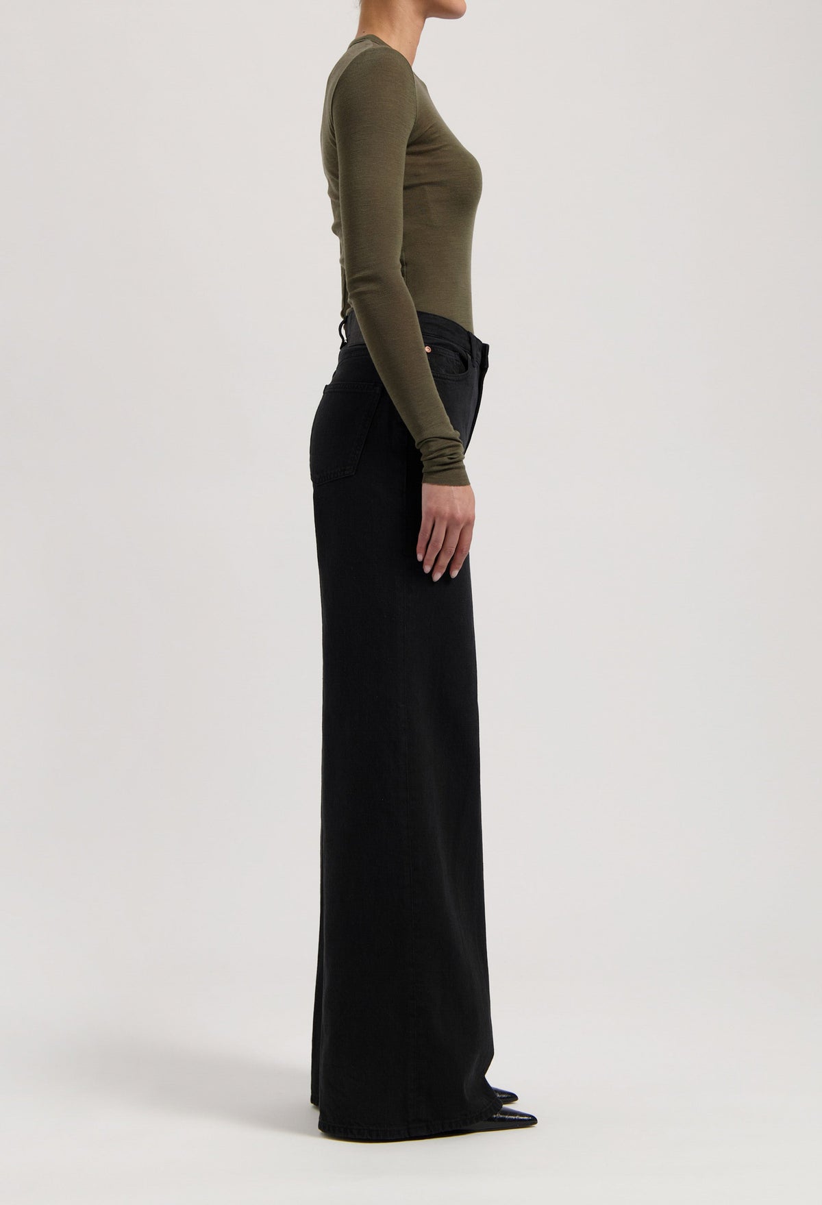 Side view of a model wearing high-waisted black wide-leg pants paired with an olive green long-sleeve fitted top.