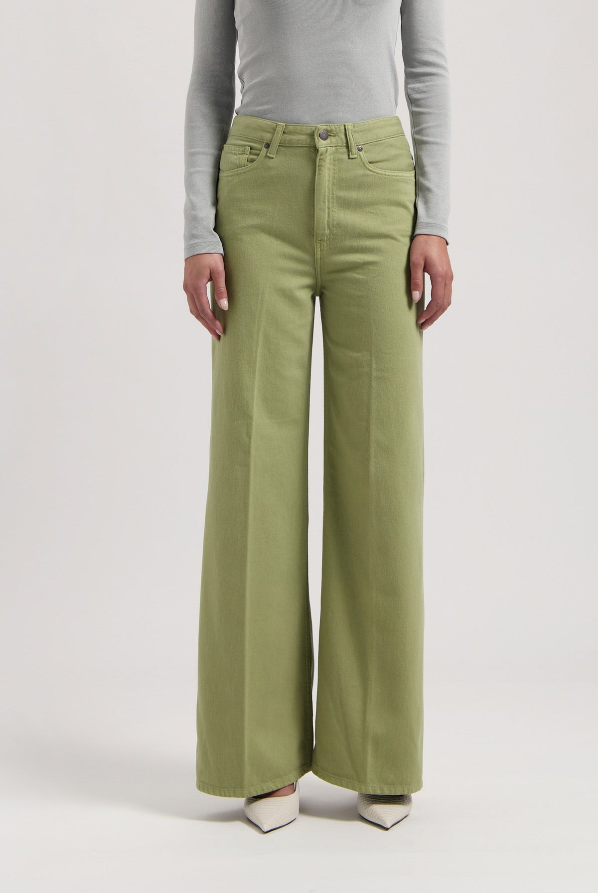 Green wide-leg jeans made from cotton, worn with a light gray long-sleeve top, showcasing a stylish casual look.