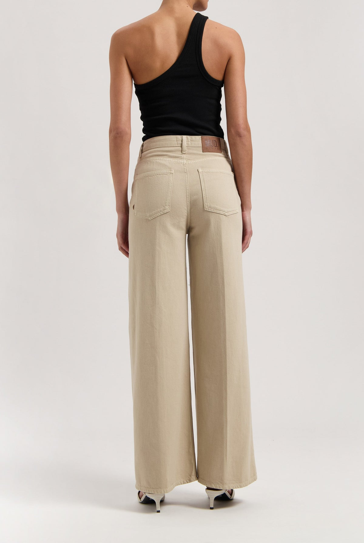 Wide-leg beige trousers in a minimalist design, paired with a black asymmetrical sleeveless top, showcasing modern casualwear.