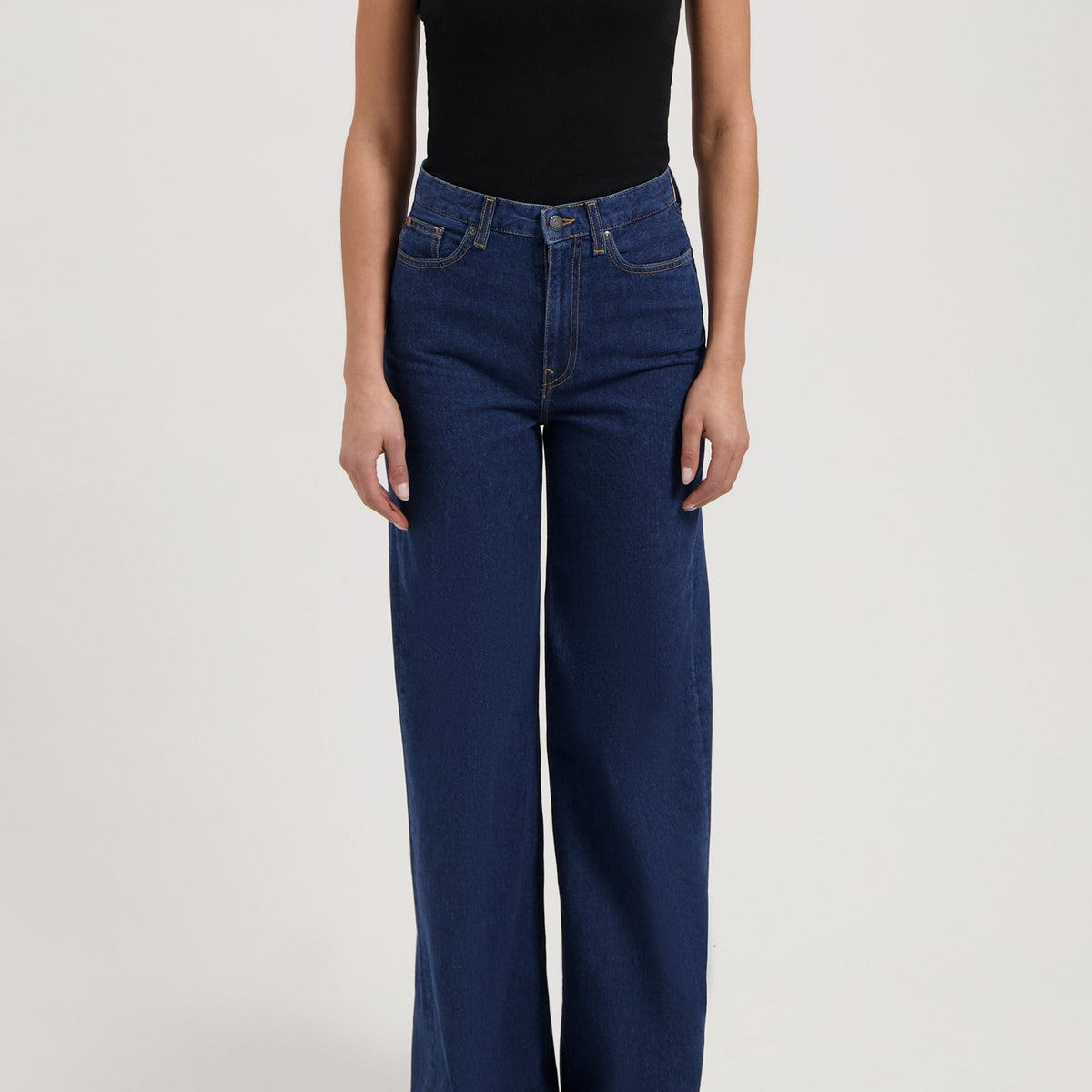 Wide-leg high-waisted jeans in deep blue, paired with a black one-shoulder top, showing a casual yet stylish look.