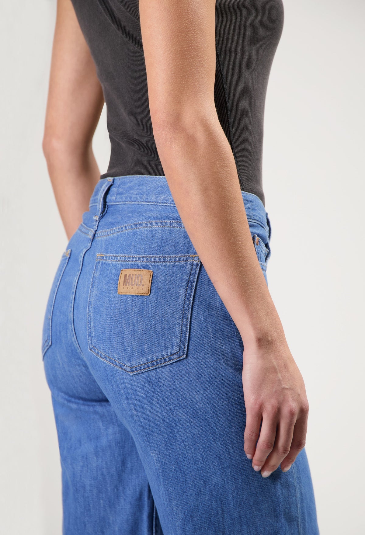 Close-up of MUD Jeans in blue denim, showcasing a high-waisted, relaxed fit style worn with a fitted black top.