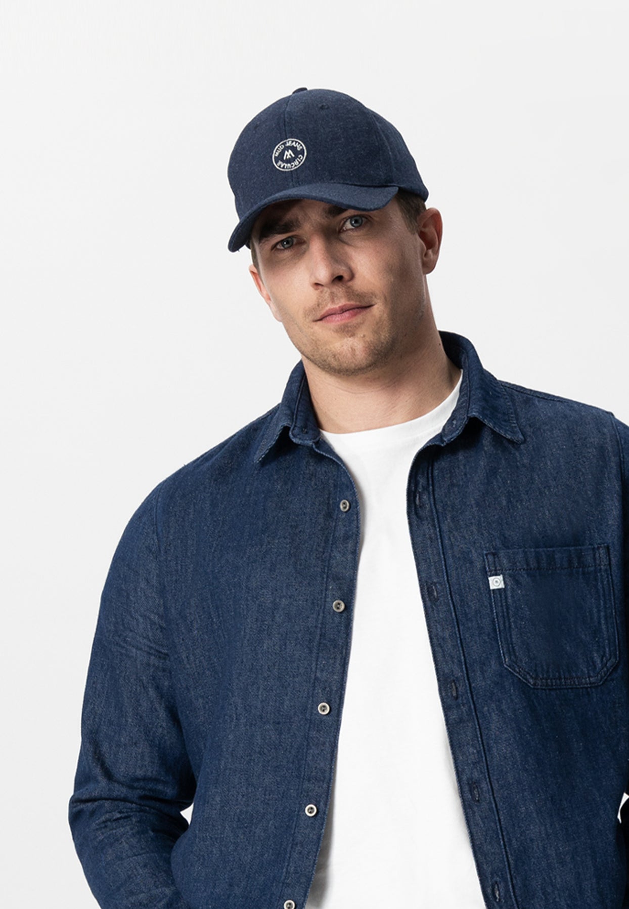 Sustainable MUD Jeans ensemble with denim apron and matching pants, styled with a hoodie and beanie, showcasing ethical fashion.