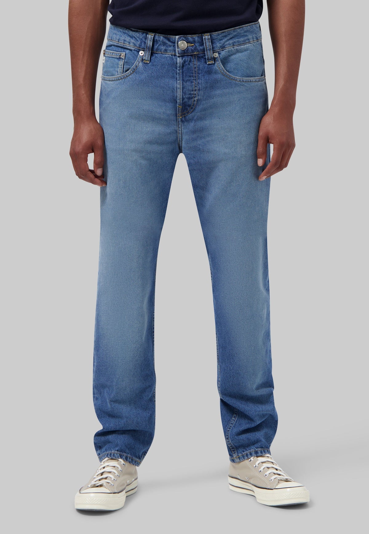Sustainable MUD Jeans in dark denim, crafted from organic cotton, styled with a simple white tee and white sneakers.
