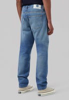 Sustainable dark denim jeans by Mud Jeans, crafted from organic cotton, modeled with a white T-shirt and white sneakers.