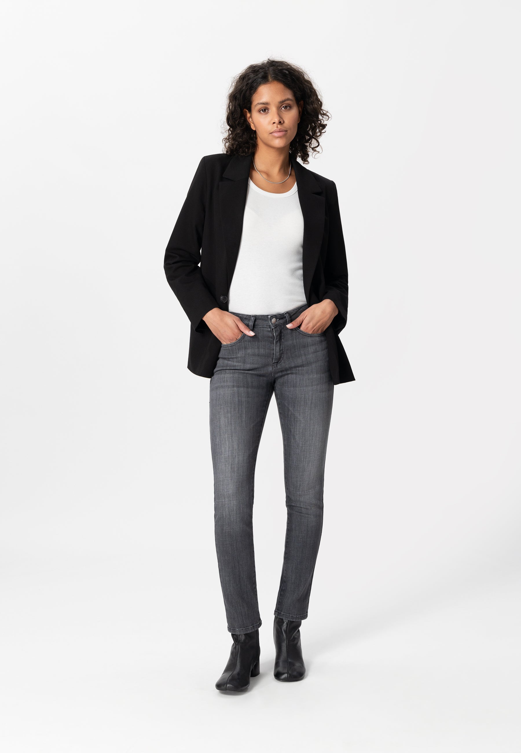 Fashion model wearing a smart black blazer, white top, and gray slim-fit jeans paired with stylish black ankle boots.