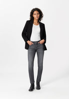 Fashion model wearing a smart black blazer, white top, and gray slim-fit jeans paired with stylish black ankle boots.