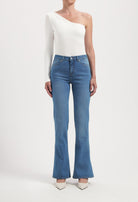 One-shoulder white top paired with blue flared jeans and white heels, showcasing minimalist fashion style.
