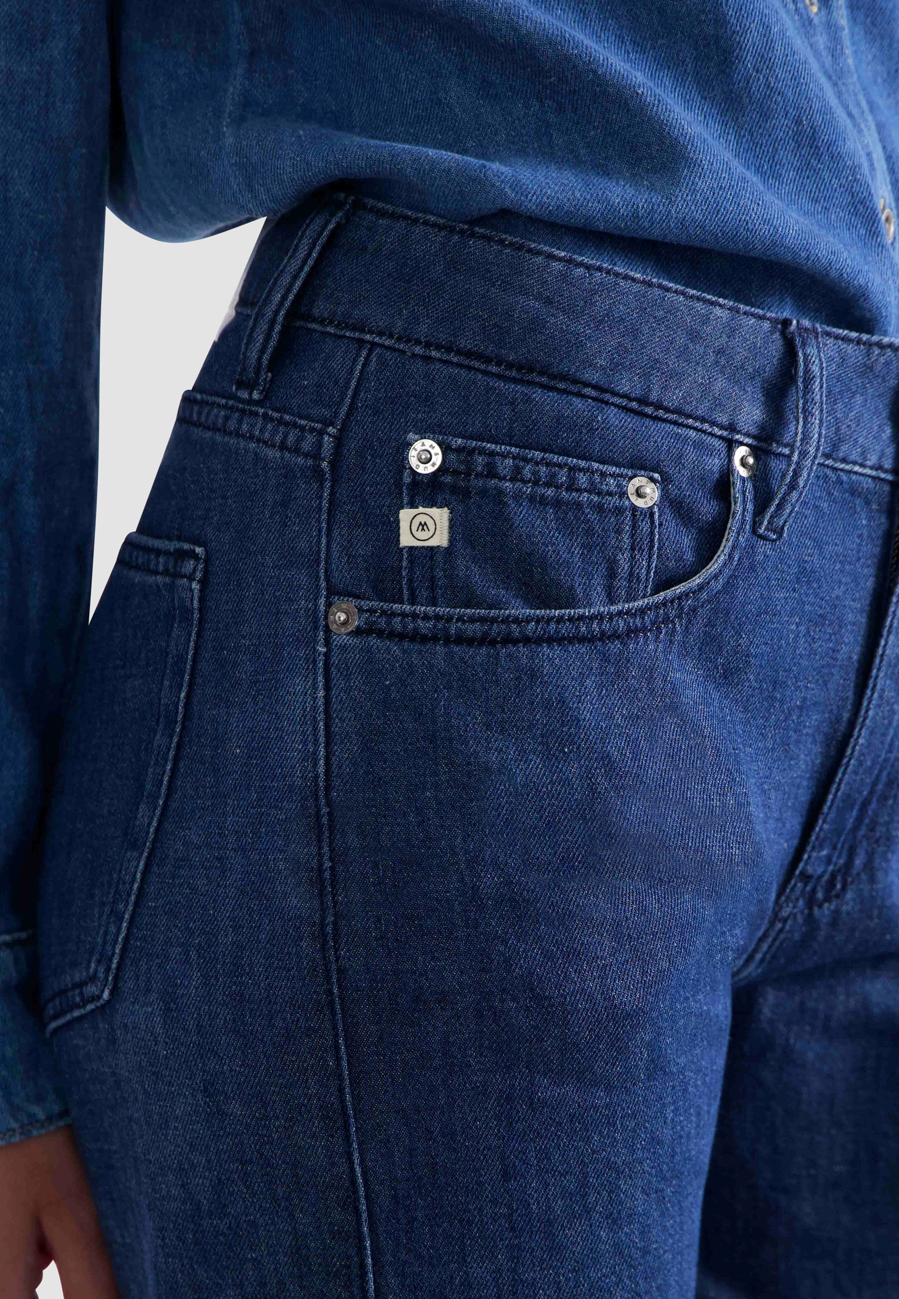 Dark blue denim jeans with silver button accents, featuring a close-up on the pocket and stitching details.