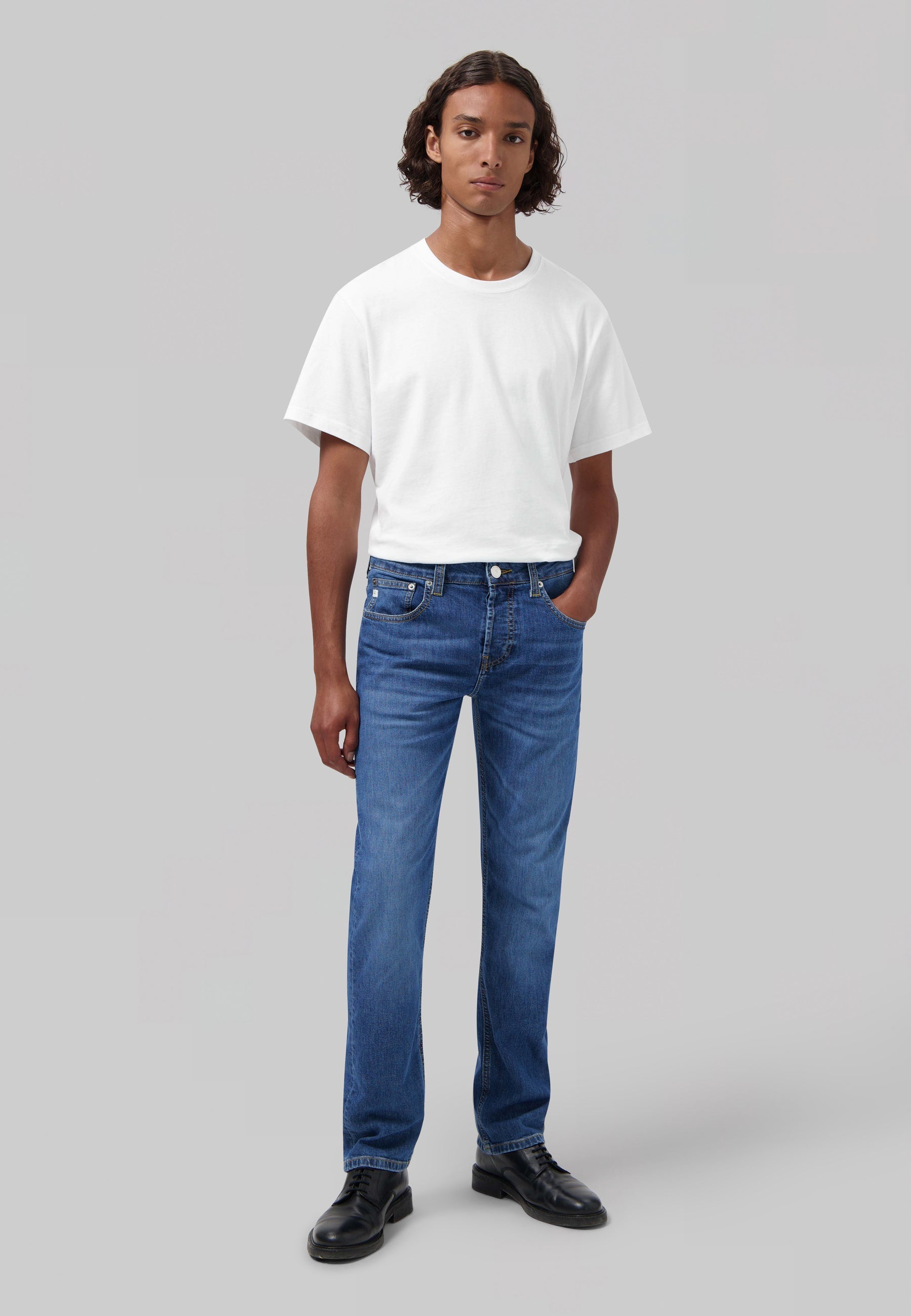 Sustainable MUD Jeans in mid-blue denim, classic fit, crafted ethically from organic materials, paired with black shoes.