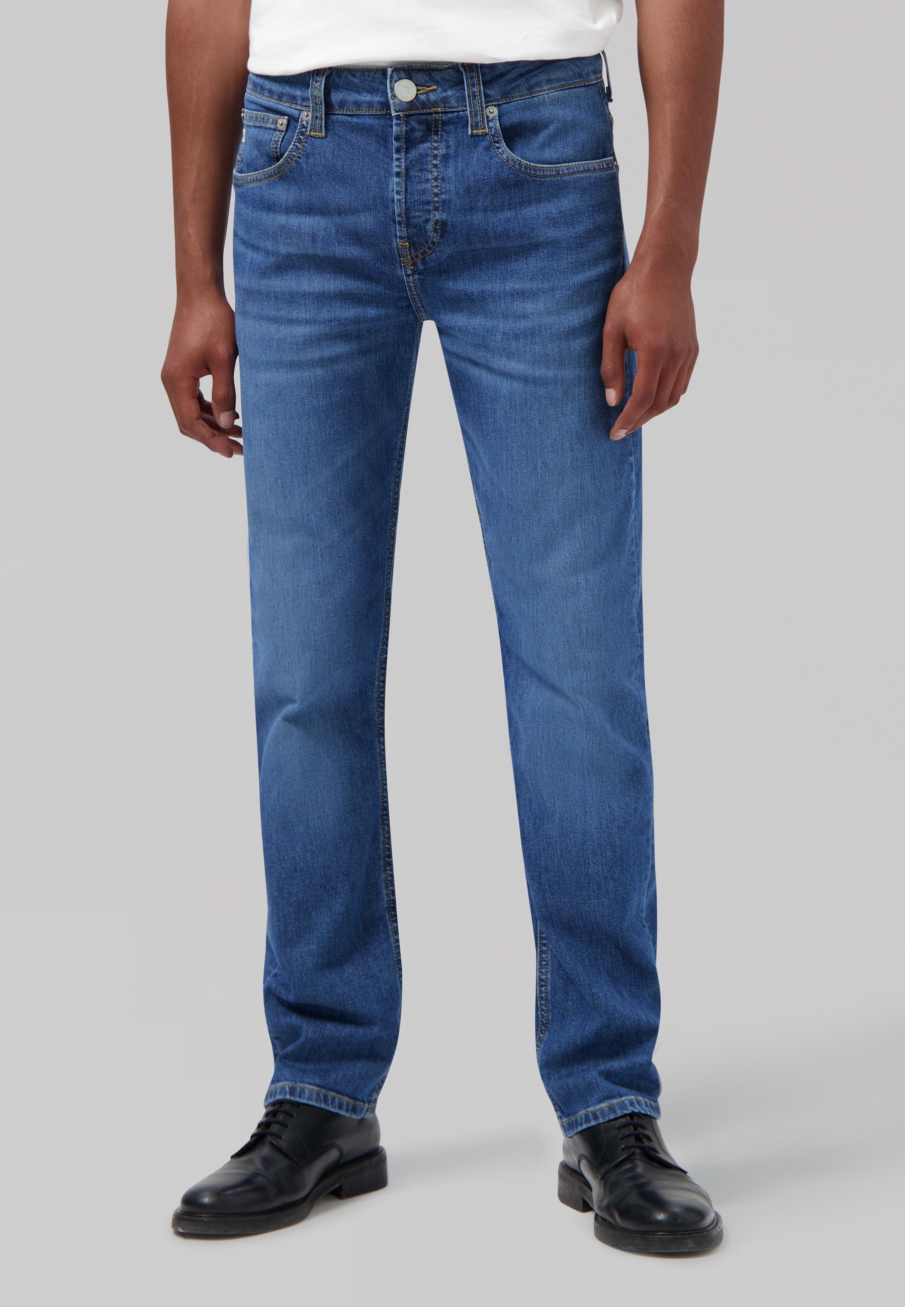 Sustainable MUD Jeans made from organic cotton in classic blue denim, paired with a white tee and black shoes.