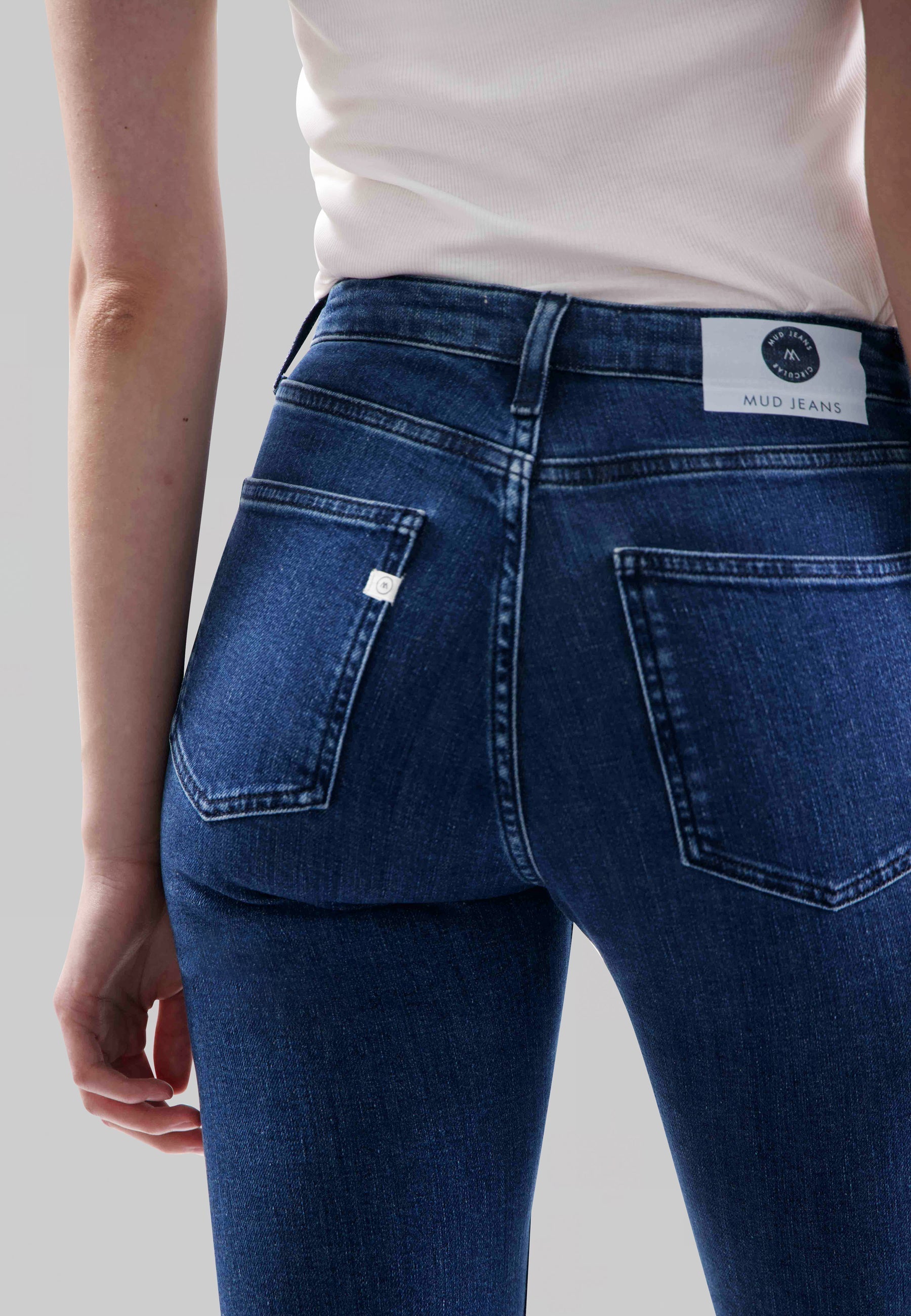Back view of MUD Jeans made from organic cotton, showcasing blue slim-fit denim worn with a white sleeveless top.