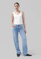 Woman wearing light blue wide-leg jeans with a fitted white tank top and black pointed shoes.