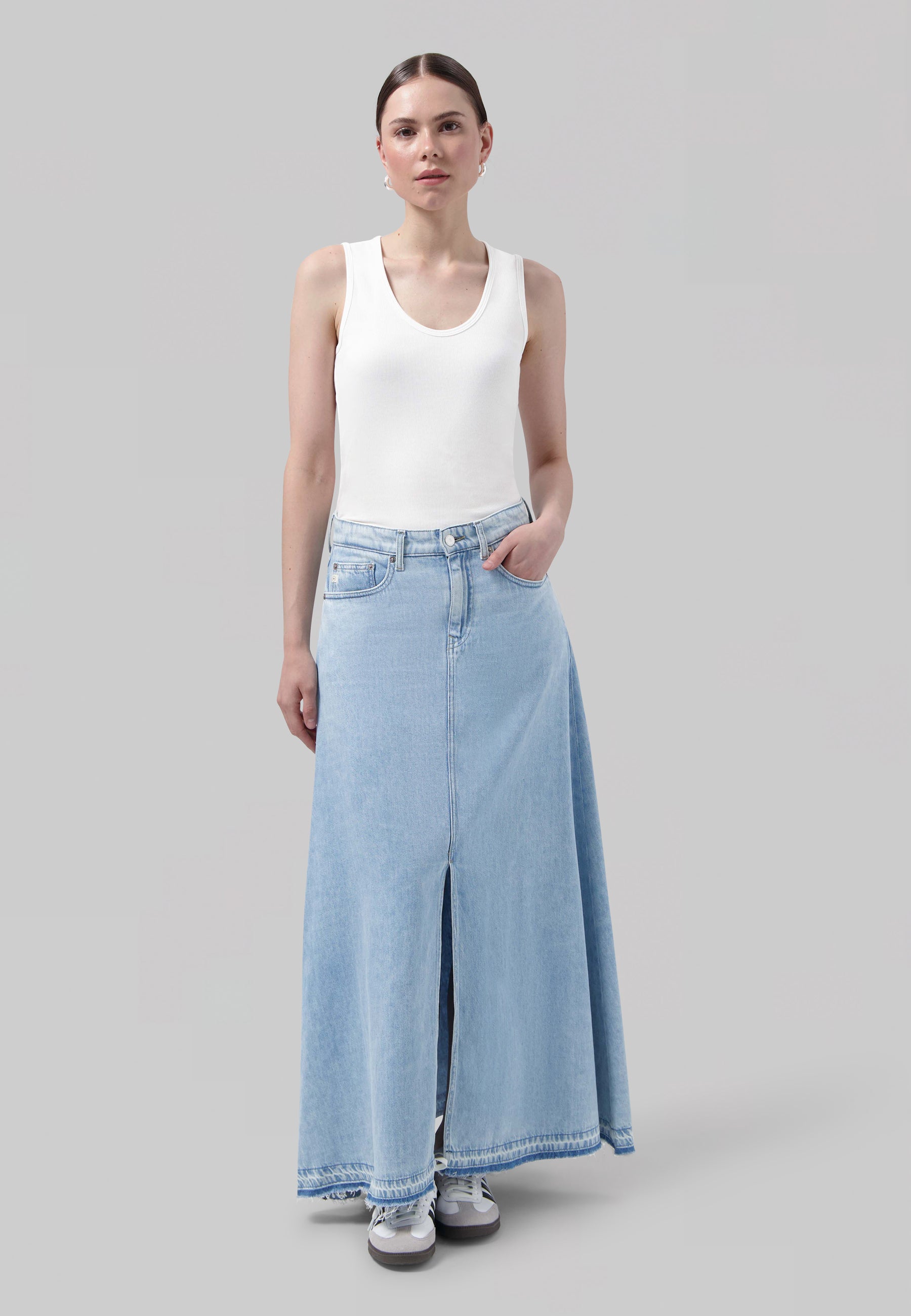 Stylish light blue denim maxi skirt with front slit, paired with a white sleeveless top, showcasing casual elegance.