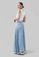 Model wearing light blue wide-leg denim jeans with frayed hems, paired with a sleeveless white tank top and black-striped sneakers.
