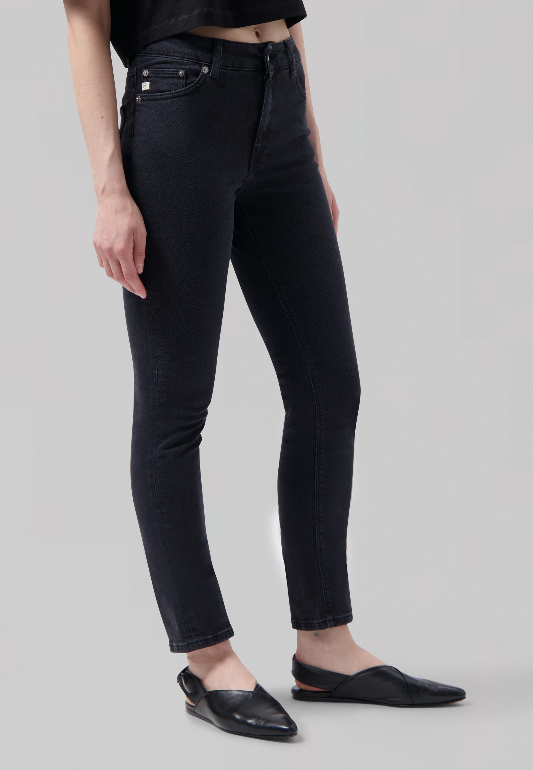 Woman wearing black high-waisted skinny jeans with casual black flats and a cropped black top.