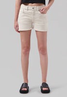 Woman wearing off-white denim shorts with a high-waist fit, styled with a cropped black top and black leather slide sandals.