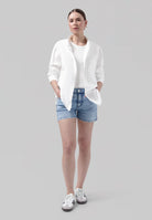 Casual summer outfit featuring light blue denim shorts, white shirt, and sneakers, perfect for a relaxed, stylish look.