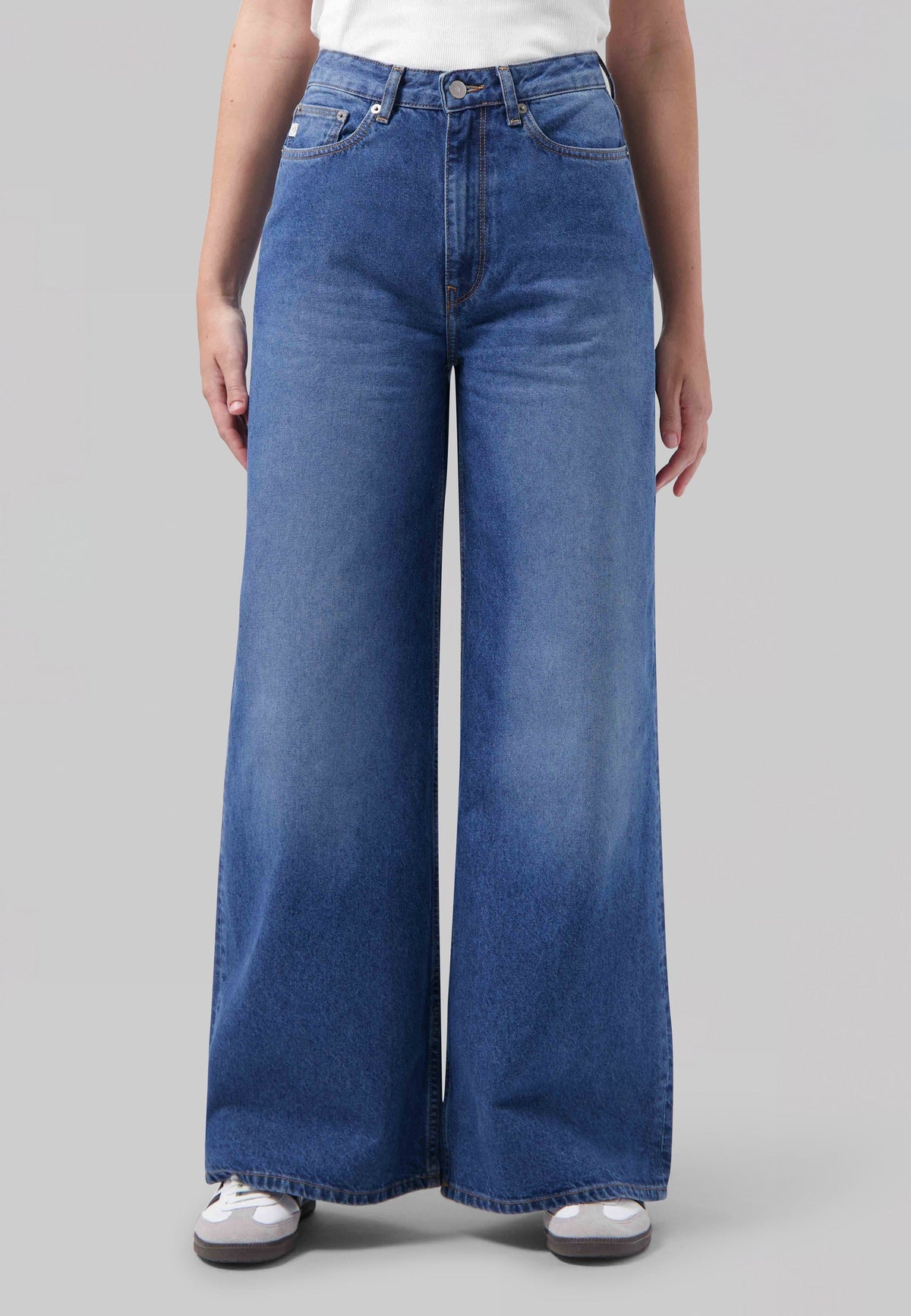 Wide-leg blue denim jeans with a high waist, featuring a classic five-pocket design, paired with a white top and sneakers.