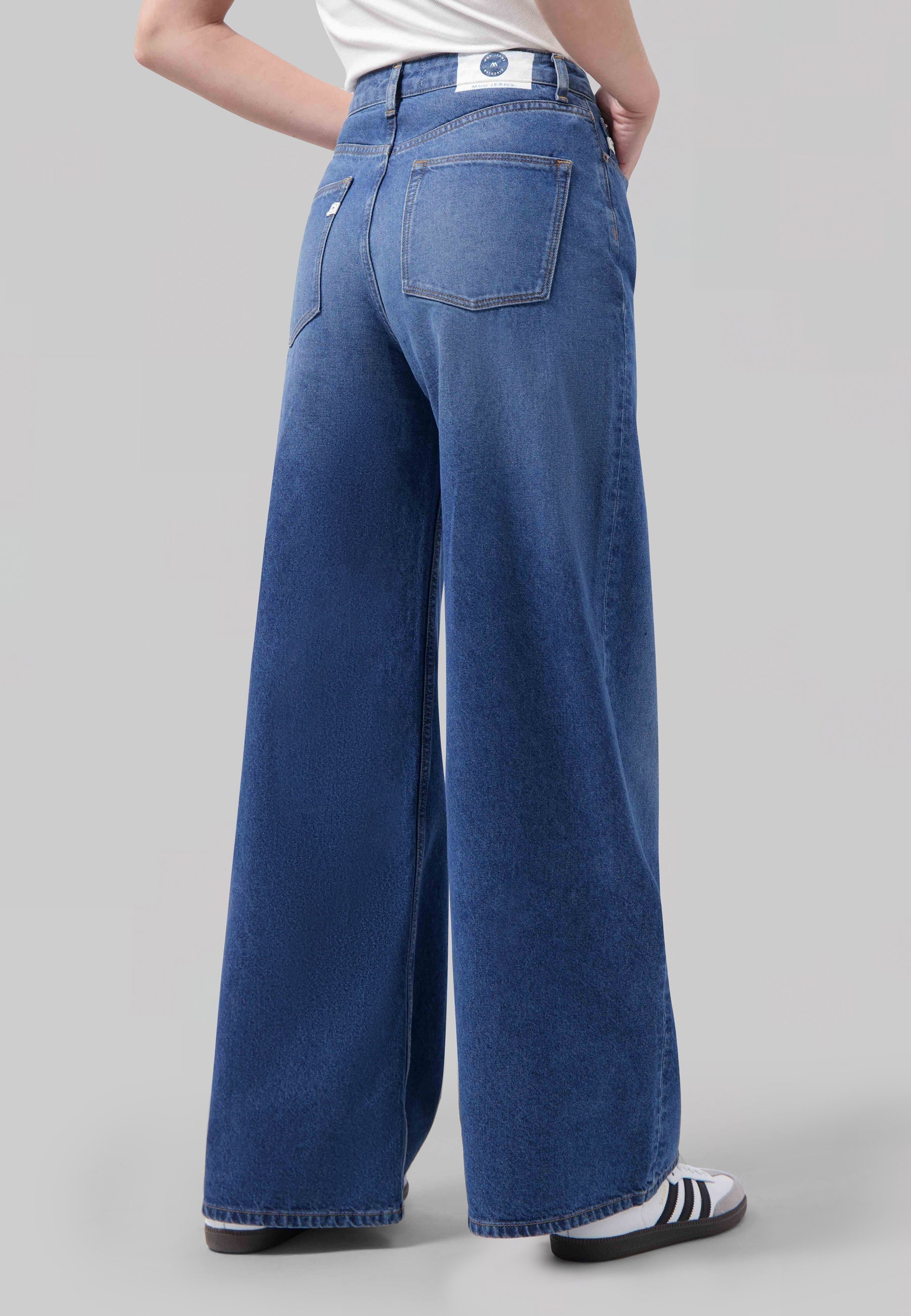 High-waisted blue wide-leg jeans made from organic cotton, paired with a casual white top and striped sneakers.