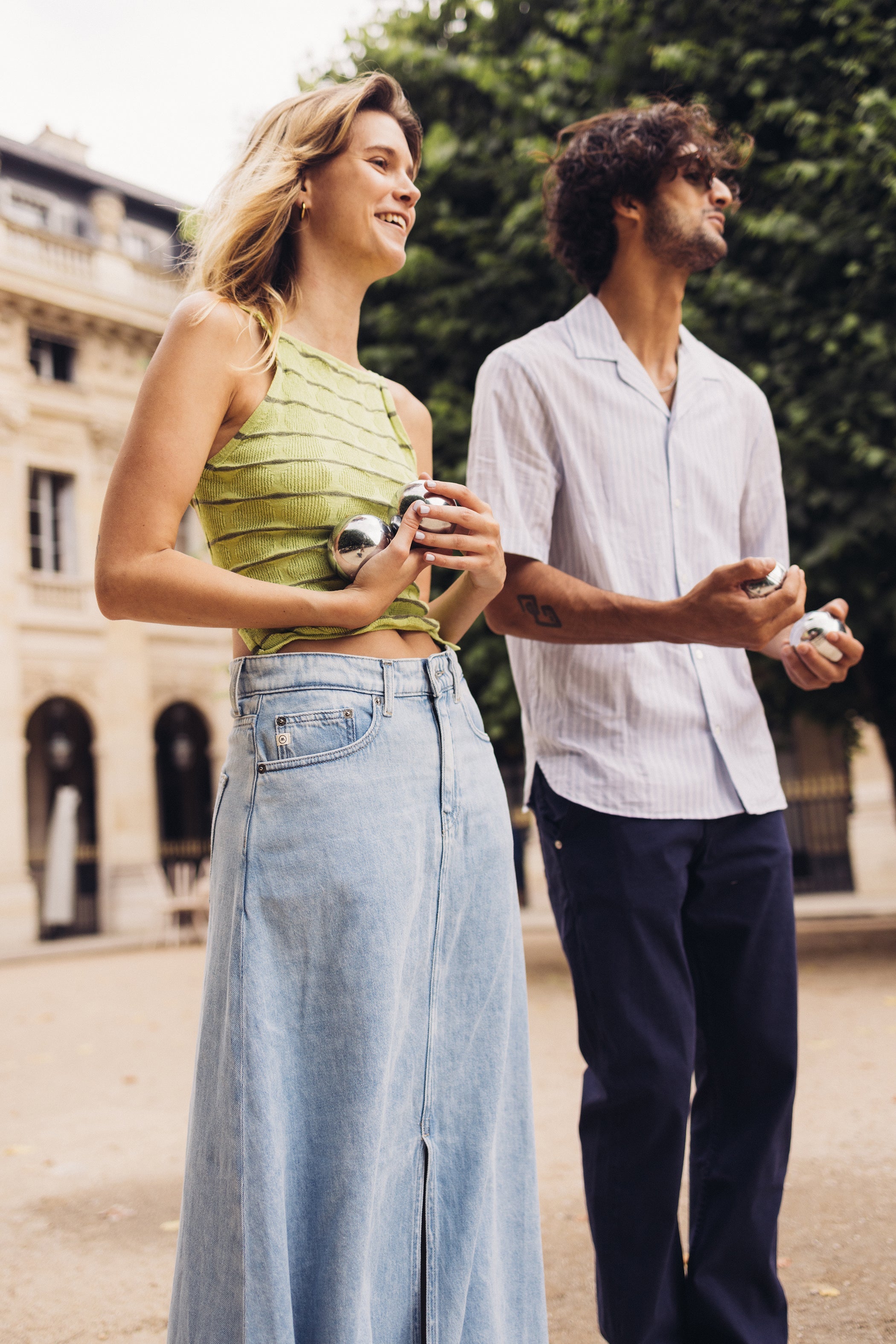 Casual summer fashion with woman in green textured top and light denim skirt beside man in striped white shirt.
