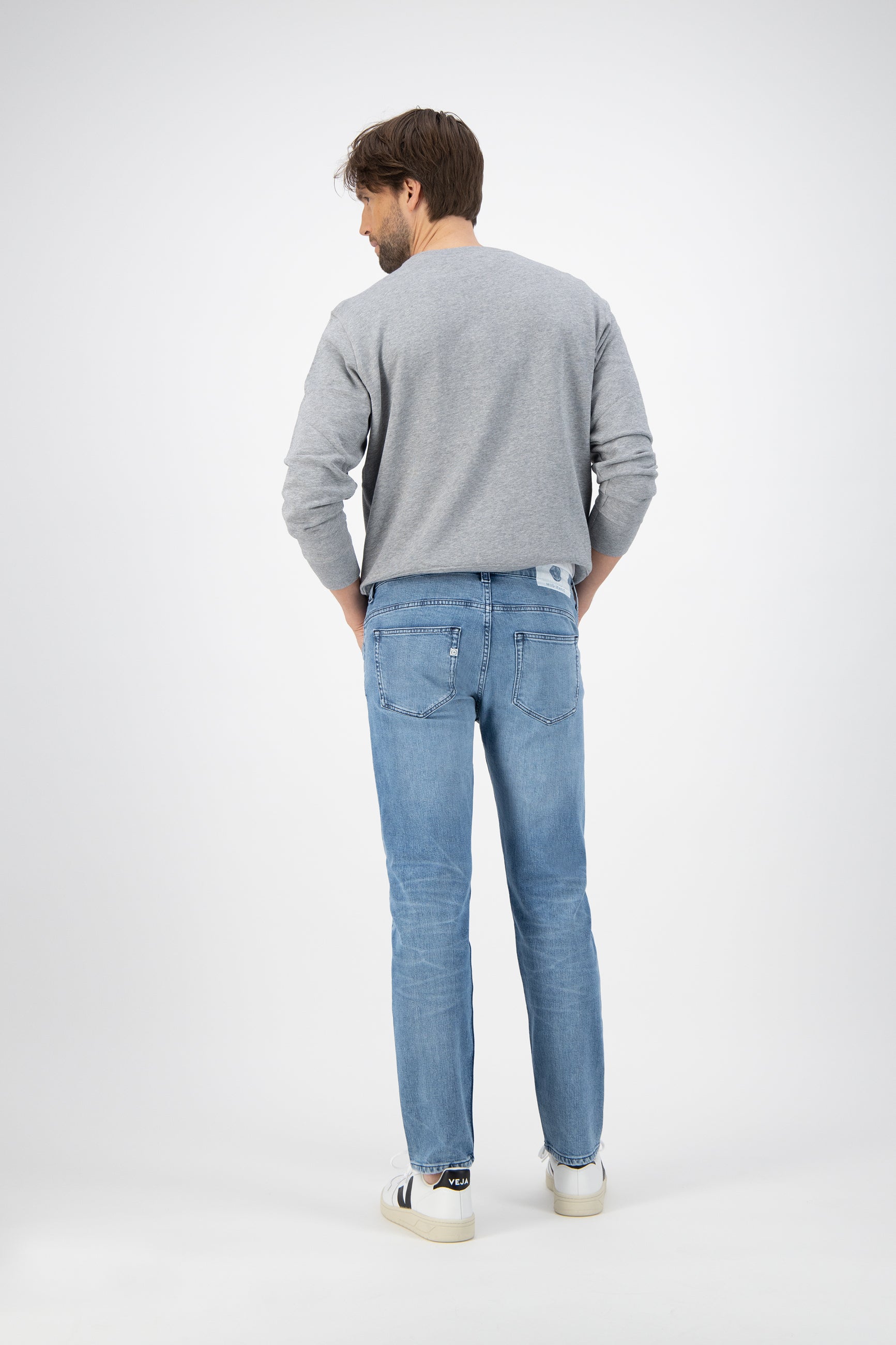 Sustainable MUD Jeans in deep indigo denim, classic straight fit, showcasing ethical fashion choices with casual white sneakers.
