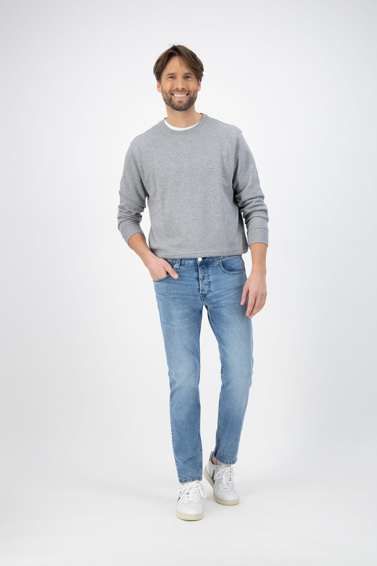 Sustainable MUD Jeans in light blue denim, classic fit, paired with a gray sweater and white sneakers.
