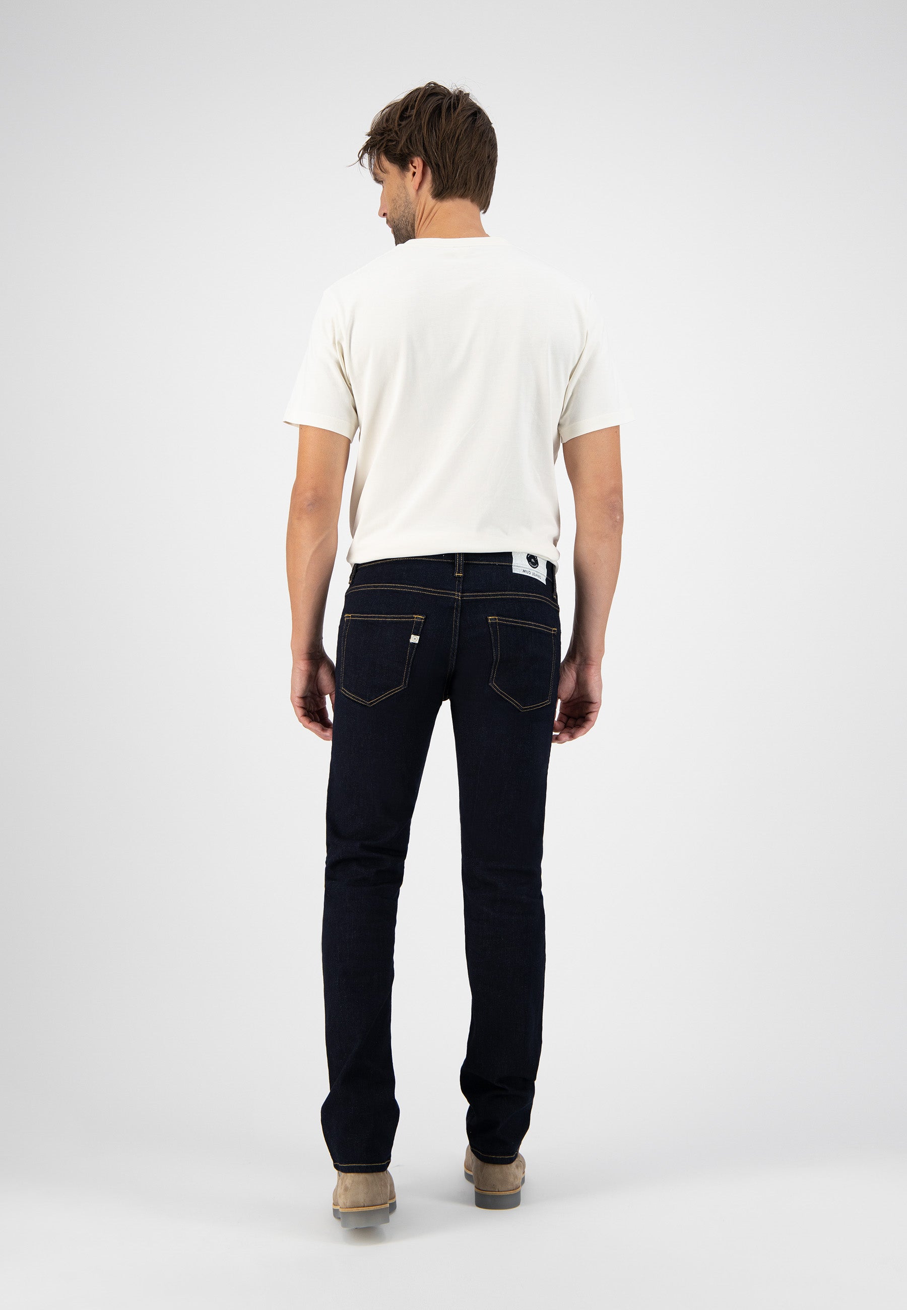 Sustainable MUD Jeans in light blue denim, crafted from organic cotton, worn with a black shirt and brown boots.