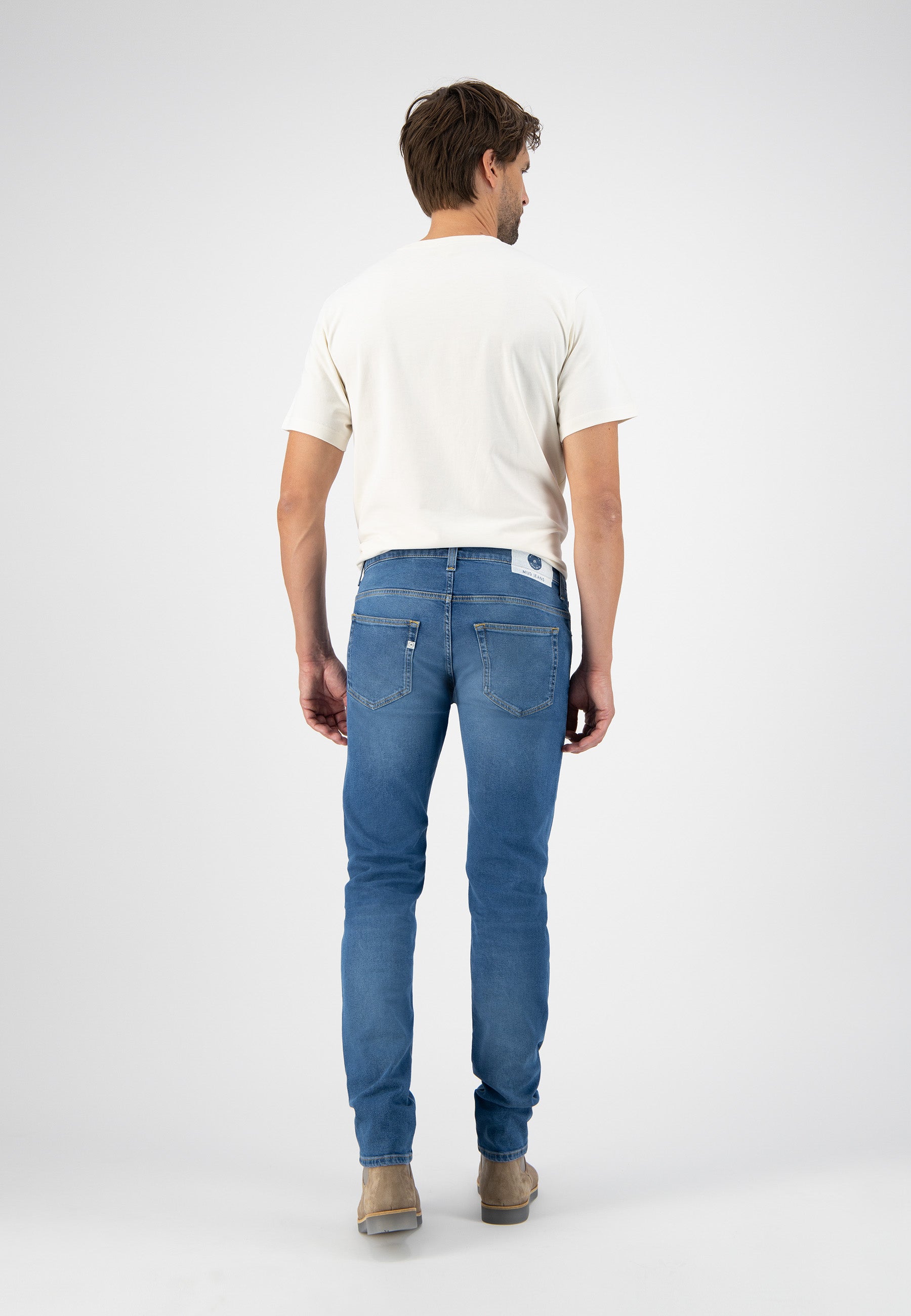 Sustainable MUD Jeans dark denim dungarees with orange logo patch, crafted from ethical materials, worn with a white shirt.