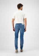 Sustainable MUD Jeans dark denim dungarees with orange logo patch, crafted from ethical materials, worn with a white shirt.