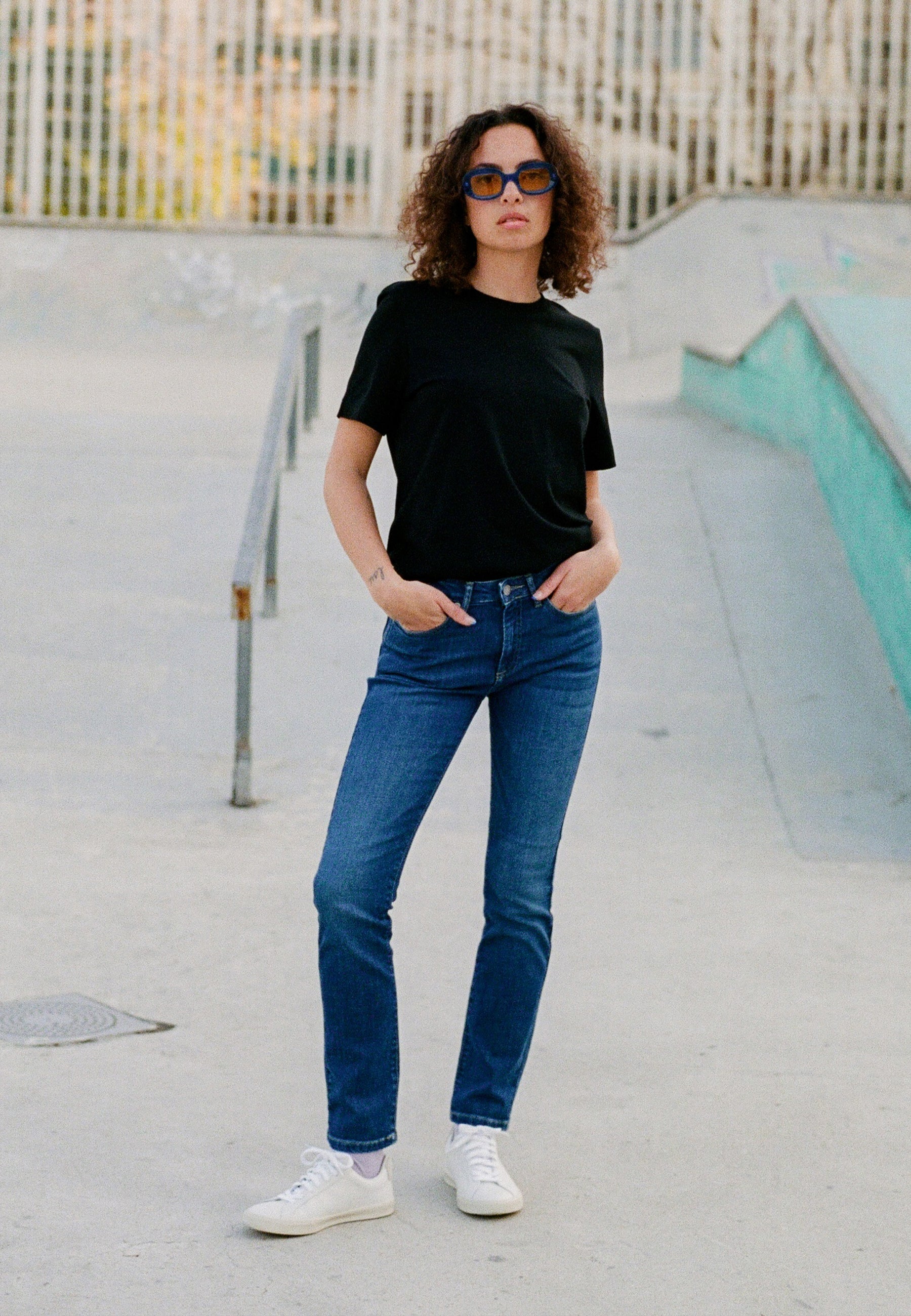 Casual urban outfit featuring a black tee, blue straight-leg jeans, and white sneakers, worn with confidence in outdoor setting.