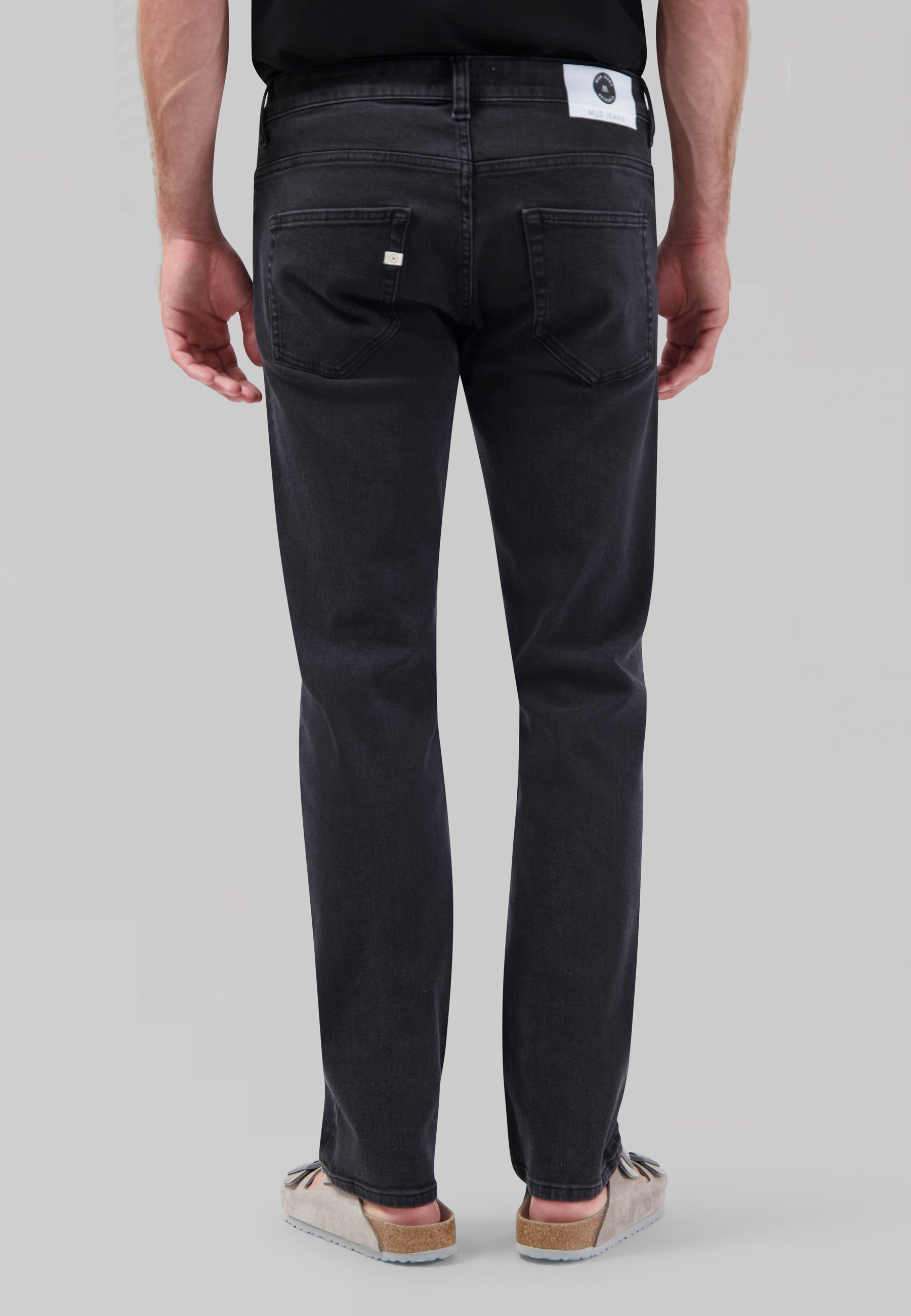 Sustainable MUD Jeans in dark blue denim, slim fit, paired with a black sweater and white sneakers for an ethical style.