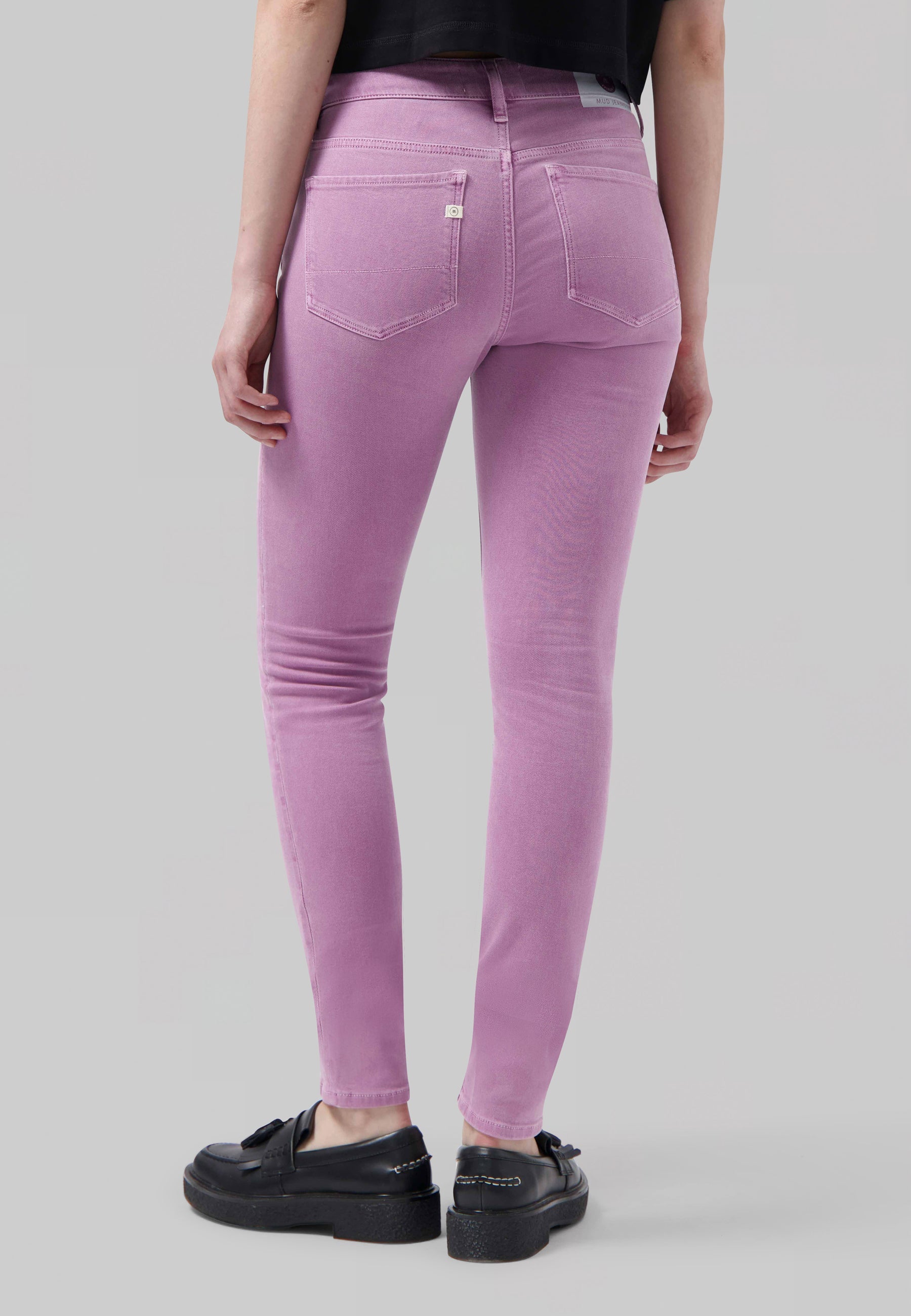 Slim-fit lavender denim jeans featuring a back pocket detail paired with a casual black top, worn with black loafers.