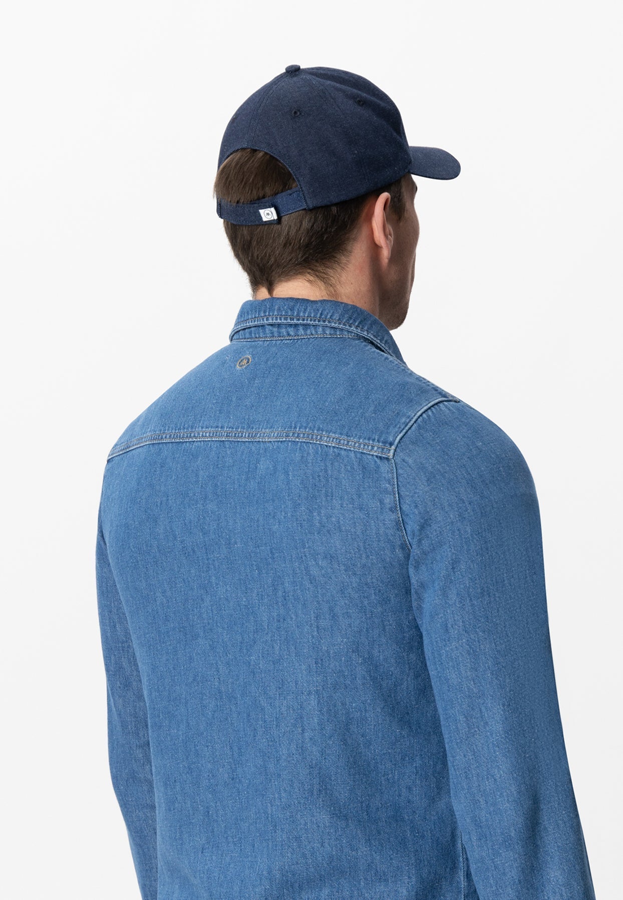 Back view of person in light blue denim jacket and navy cap, highlighting casual and classic style with detailed stitching.