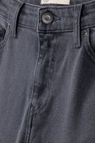 Close-up of sustainable dark gray denim jeans showcasing detailed stitching and a branded button on the waistband.