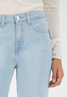 Light blue high-waisted denim jeans with a button closure, paired with a white long-sleeve top, highlighting casual style.