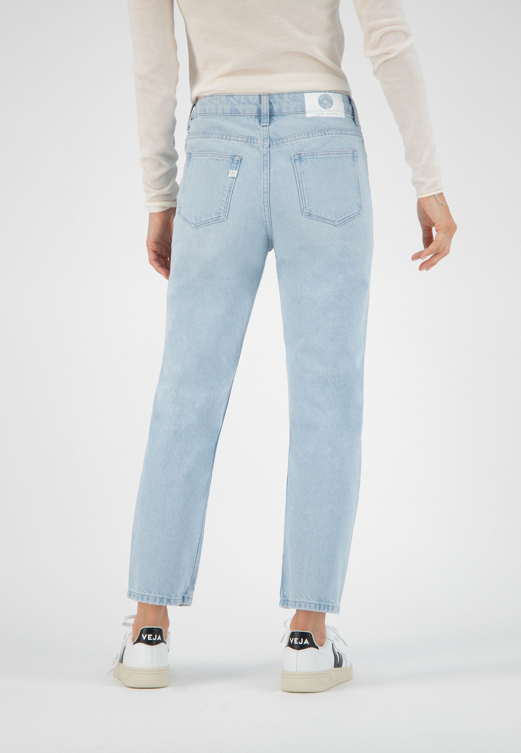 Light blue, straight-leg jeans on a person wearing a cream long-sleeve top and white sneakers with black details.