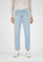 Light blue straight-leg jeans paired with a cream long-sleeve top, styled with white sneakers on a studio backdrop.