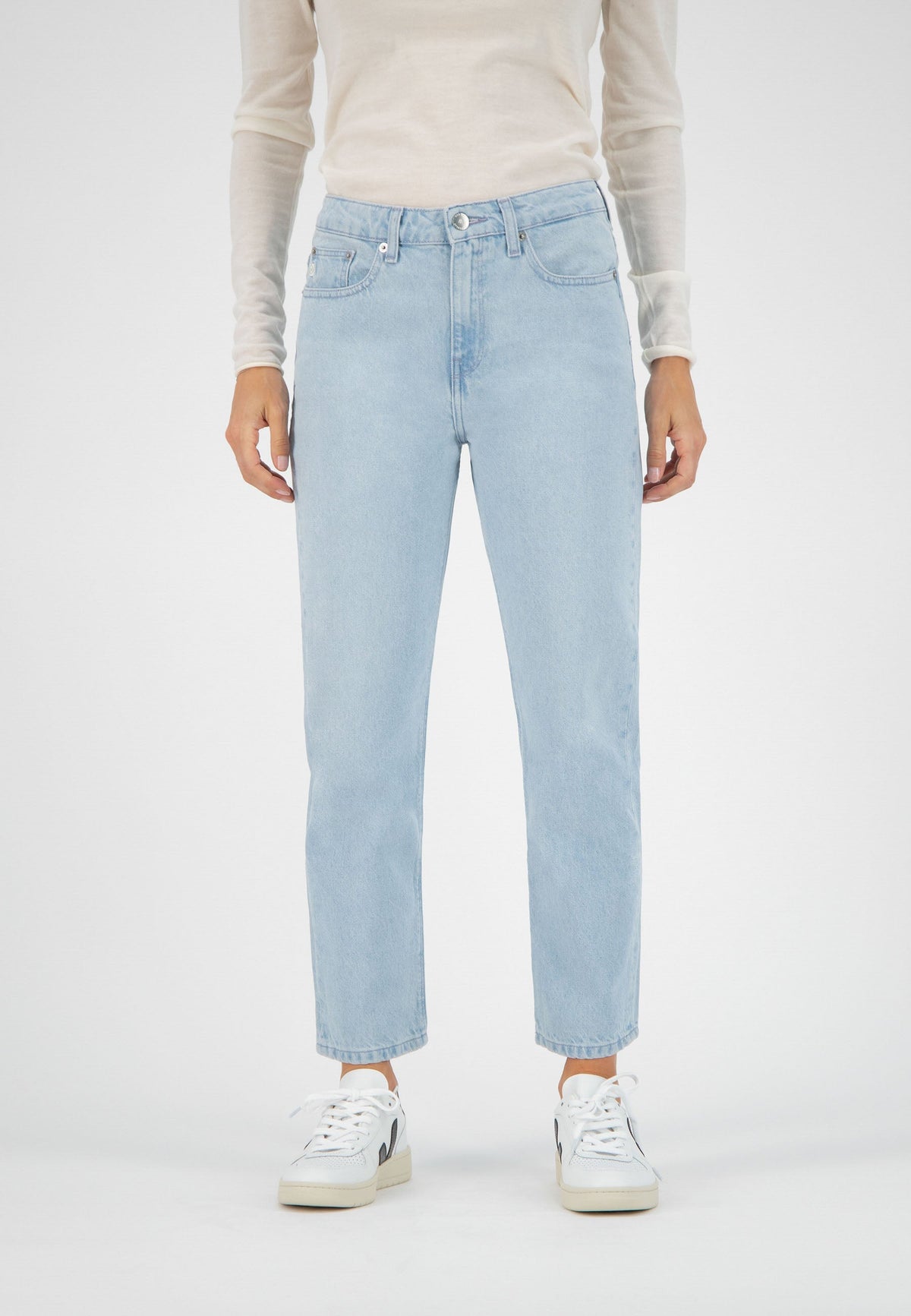 Light blue straight-leg jeans paired with a cream long-sleeve top, styled with white sneakers on a studio backdrop.