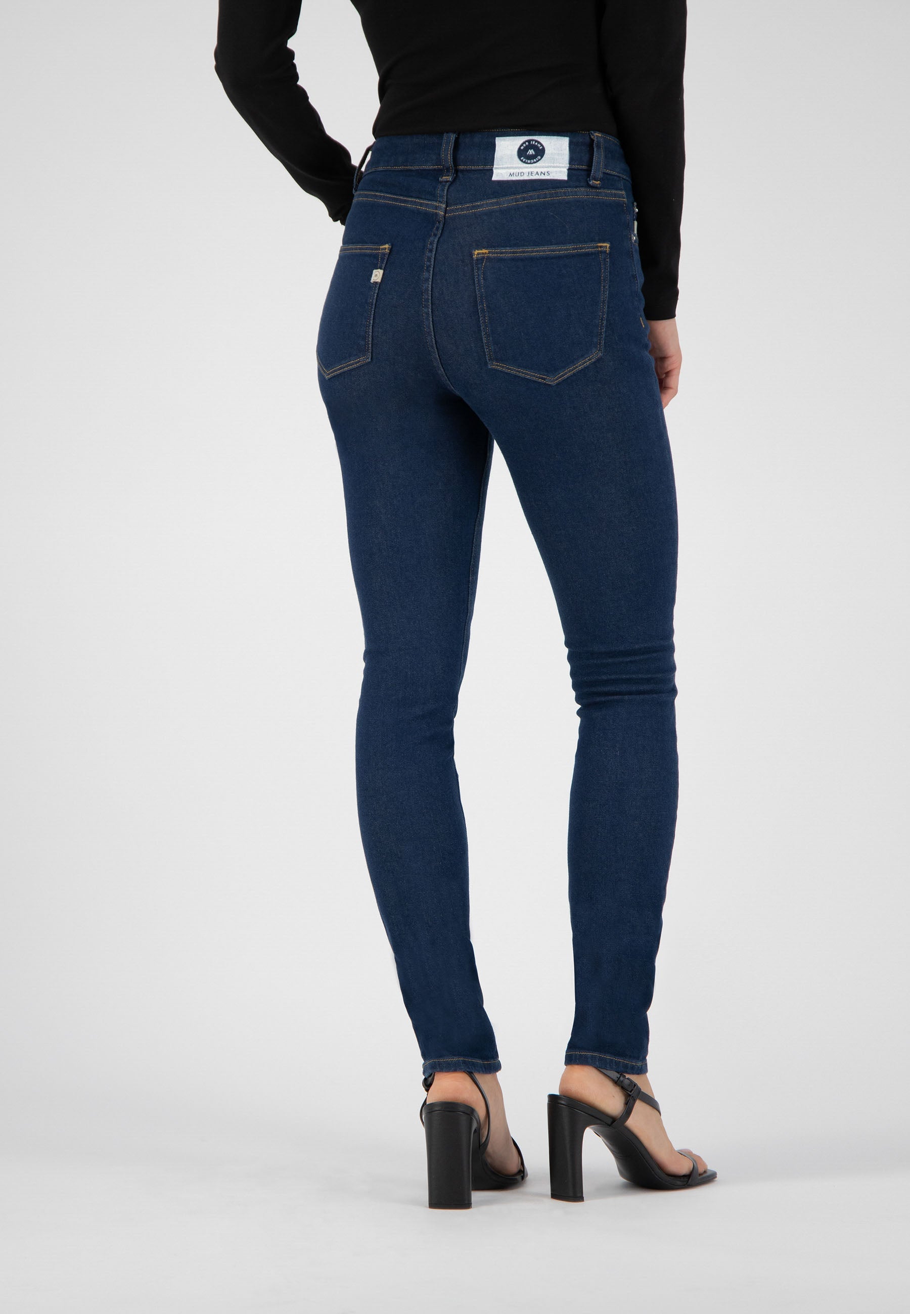 Slim-fit MUD Jeans made from organic cotton, showcasing back view of dark blue denim styled with a black long-sleeve top.
