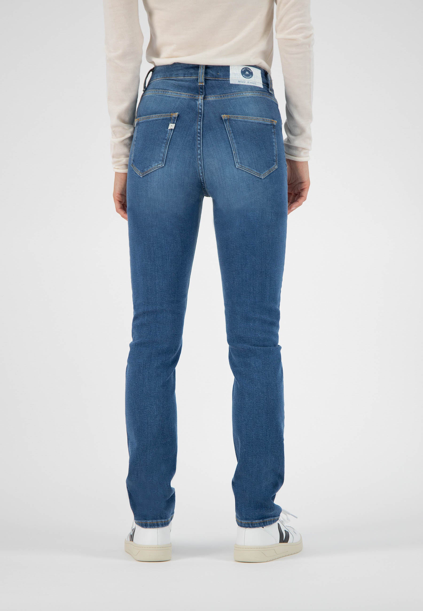 Person wearing sustainable blue skinny jeans from MUD Jeans, styled with a cream long-sleeve top, shown from the back.