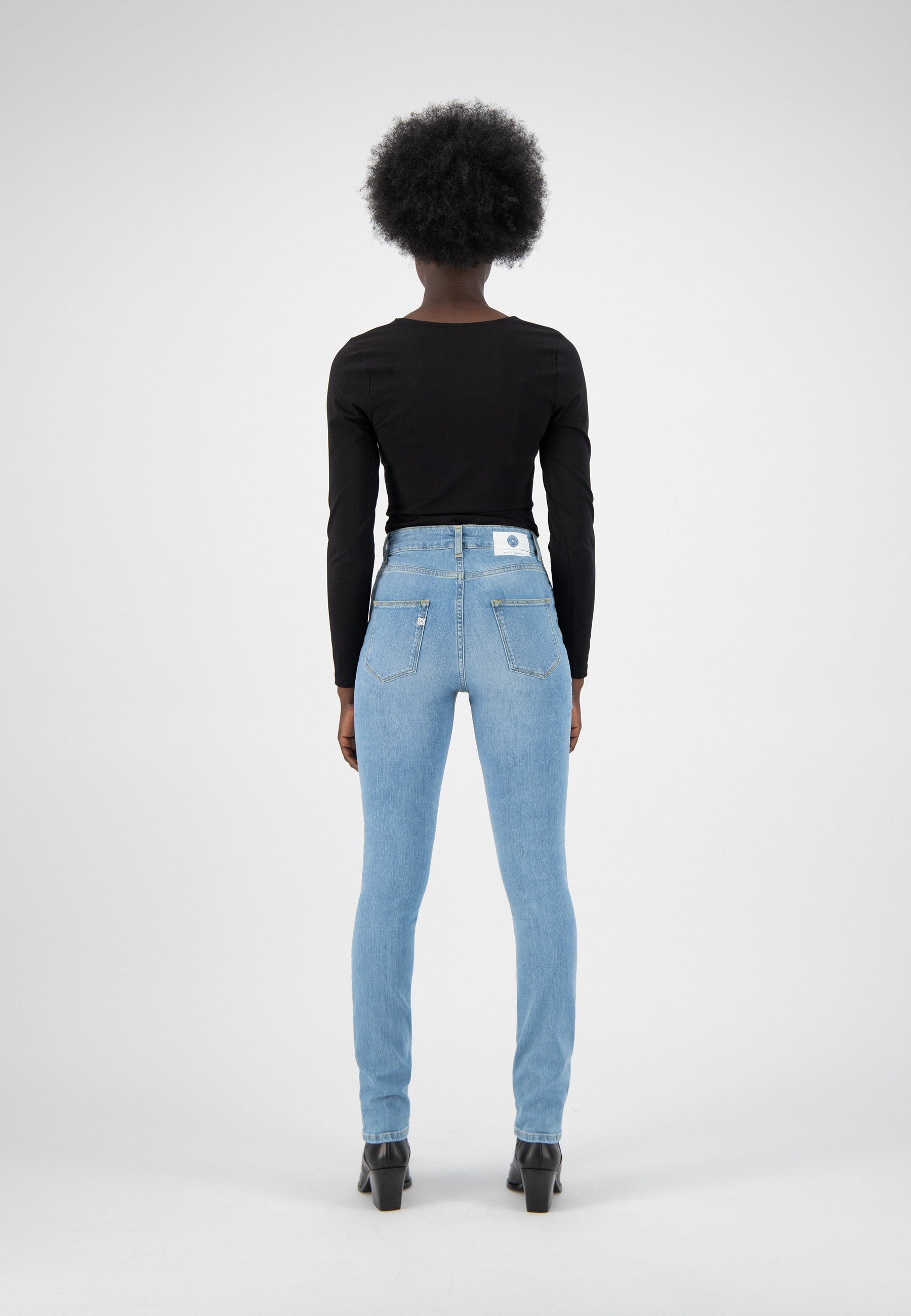 Black long-sleeve top paired with light blue high-waist skinny jeans and black ankle boots, showcasing a stylish back view.