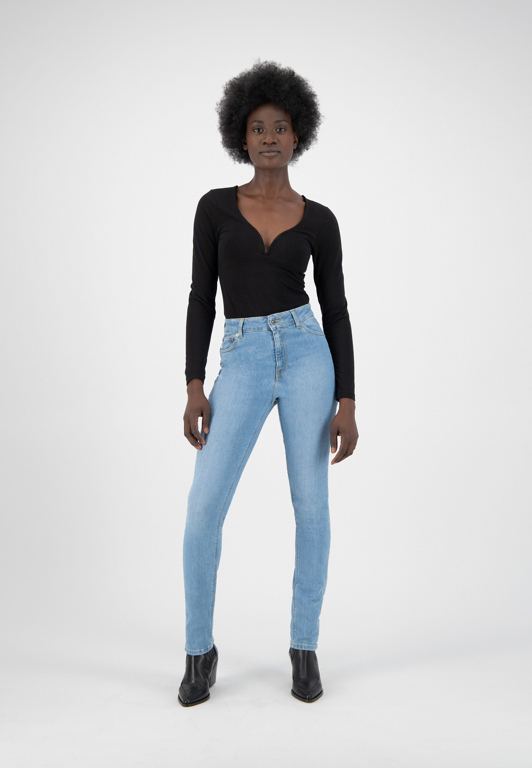 A woman wearing light blue skinny jeans paired with a black V-neck long-sleeve top and black ankle boots.