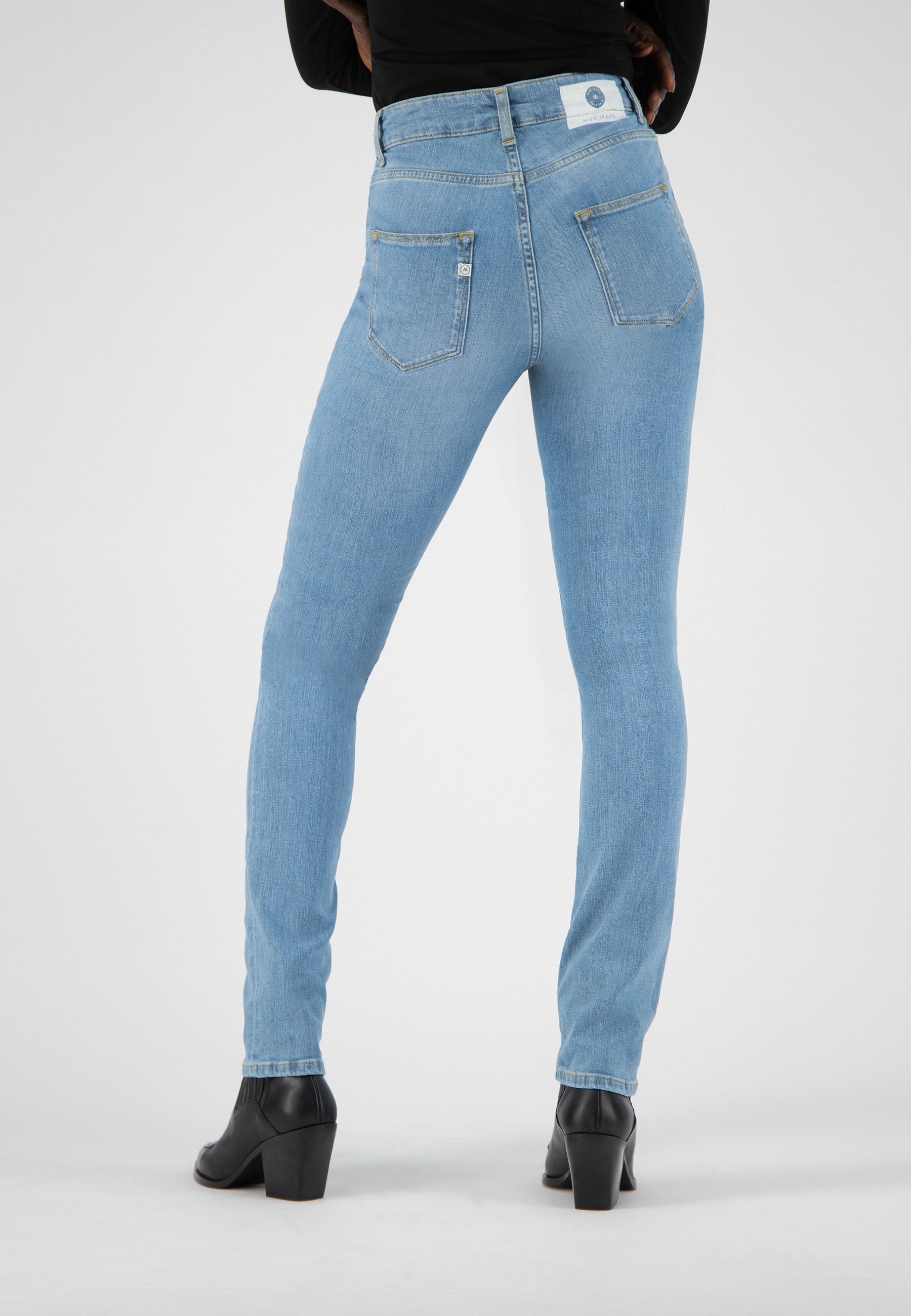 Light blue slim-fit denim jeans, featuring rear patch pockets, worn with black heeled ankle boots and a black long-sleeve top.