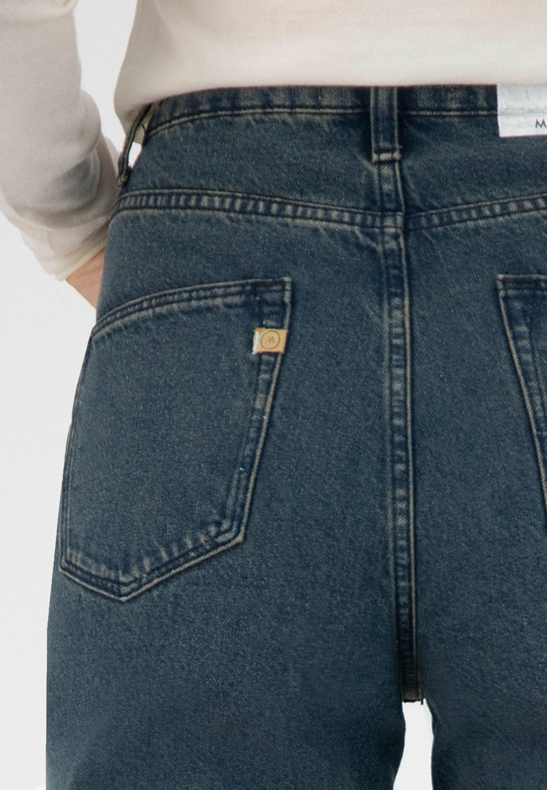 Close-up of back of dark blue organic denim jeans with visible stitching, worn with a white long-sleeve top.