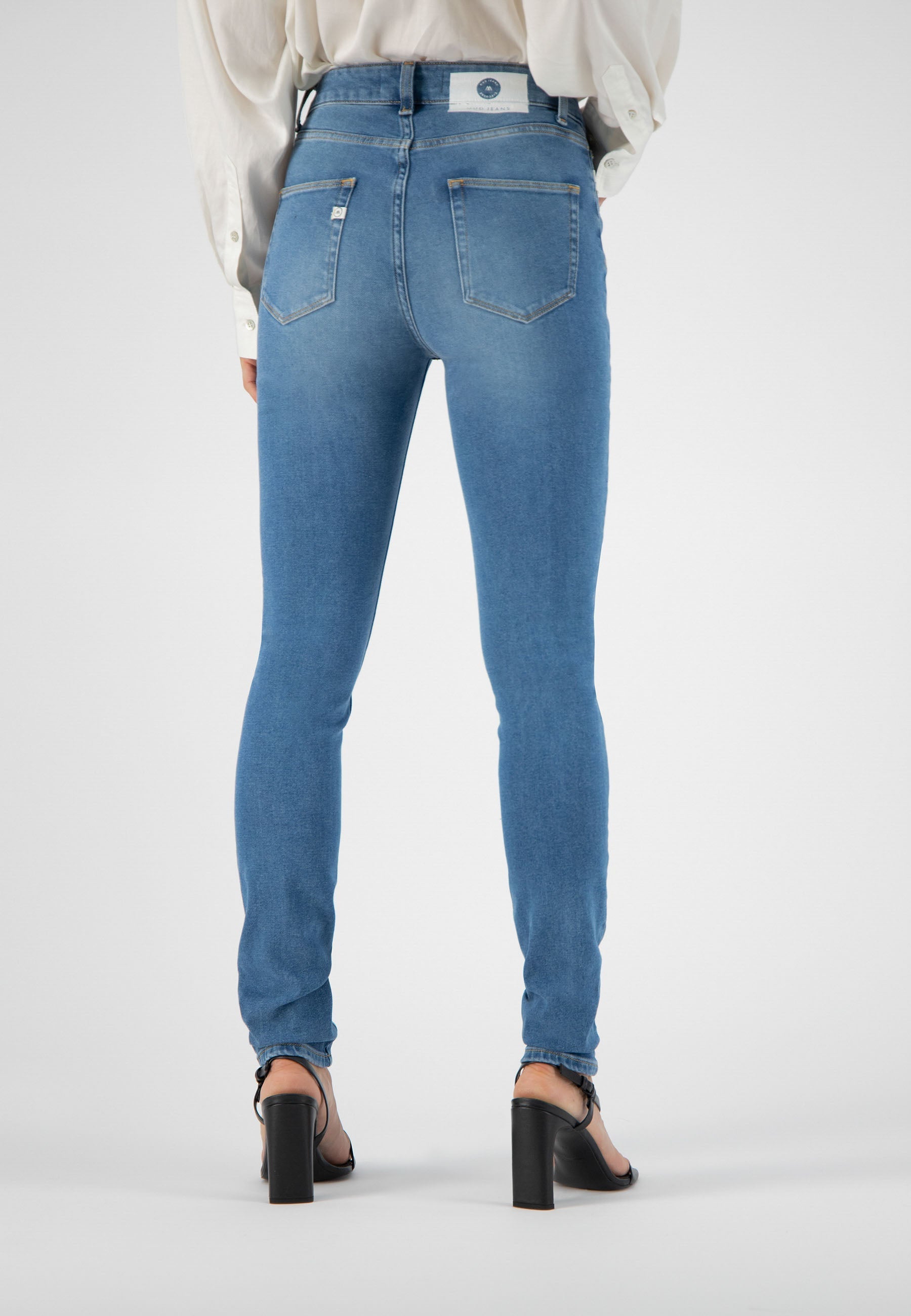 Back view of a person wearing light blue, high-waisted, slim-fit jeans paired with a white blouse and black heels.