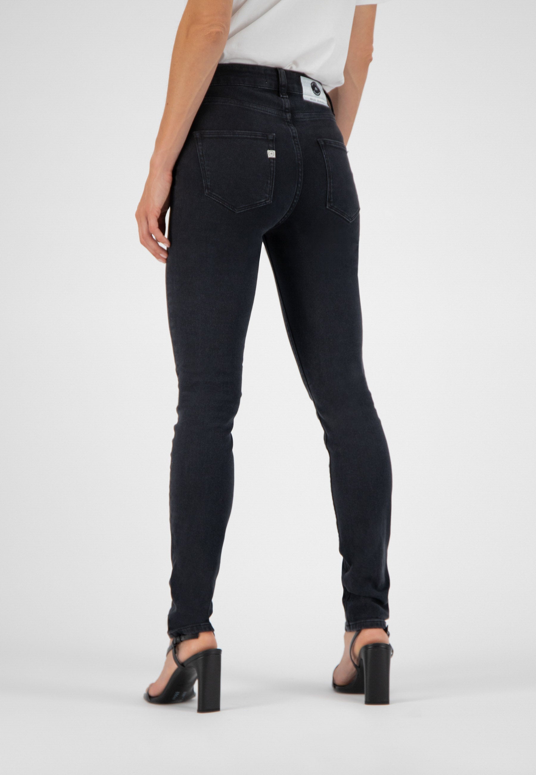 Model wearing MUD Jeans slim-fit black denim paired with a white shirt, showcasing stylish high-heeled sandals.