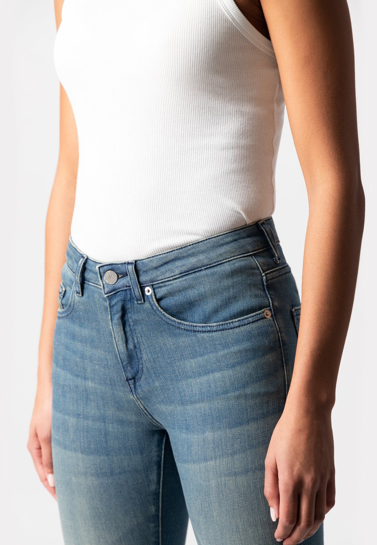 Close-up of light blue, high-waisted jeans with a slim fit, paired with a white ribbed sleeveless top, showcasing casual fashion.