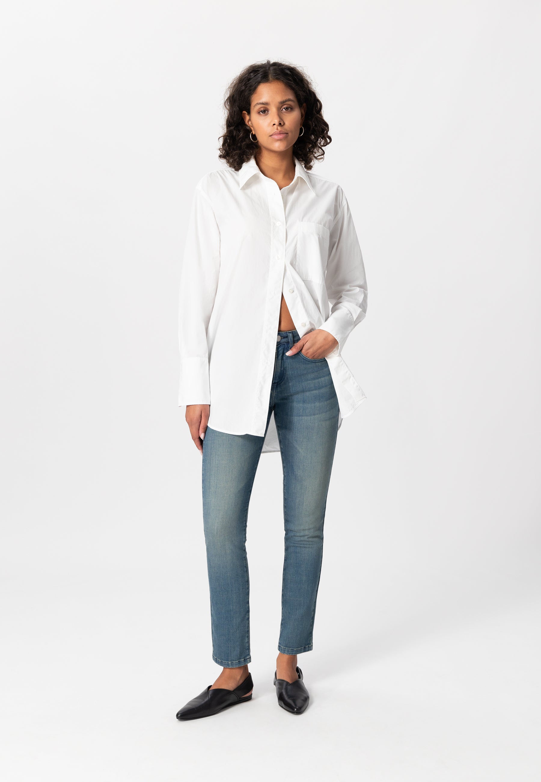 White cotton long-sleeve shirt paired with light blue slim-fit jeans and black slip-on shoes on a plain background.