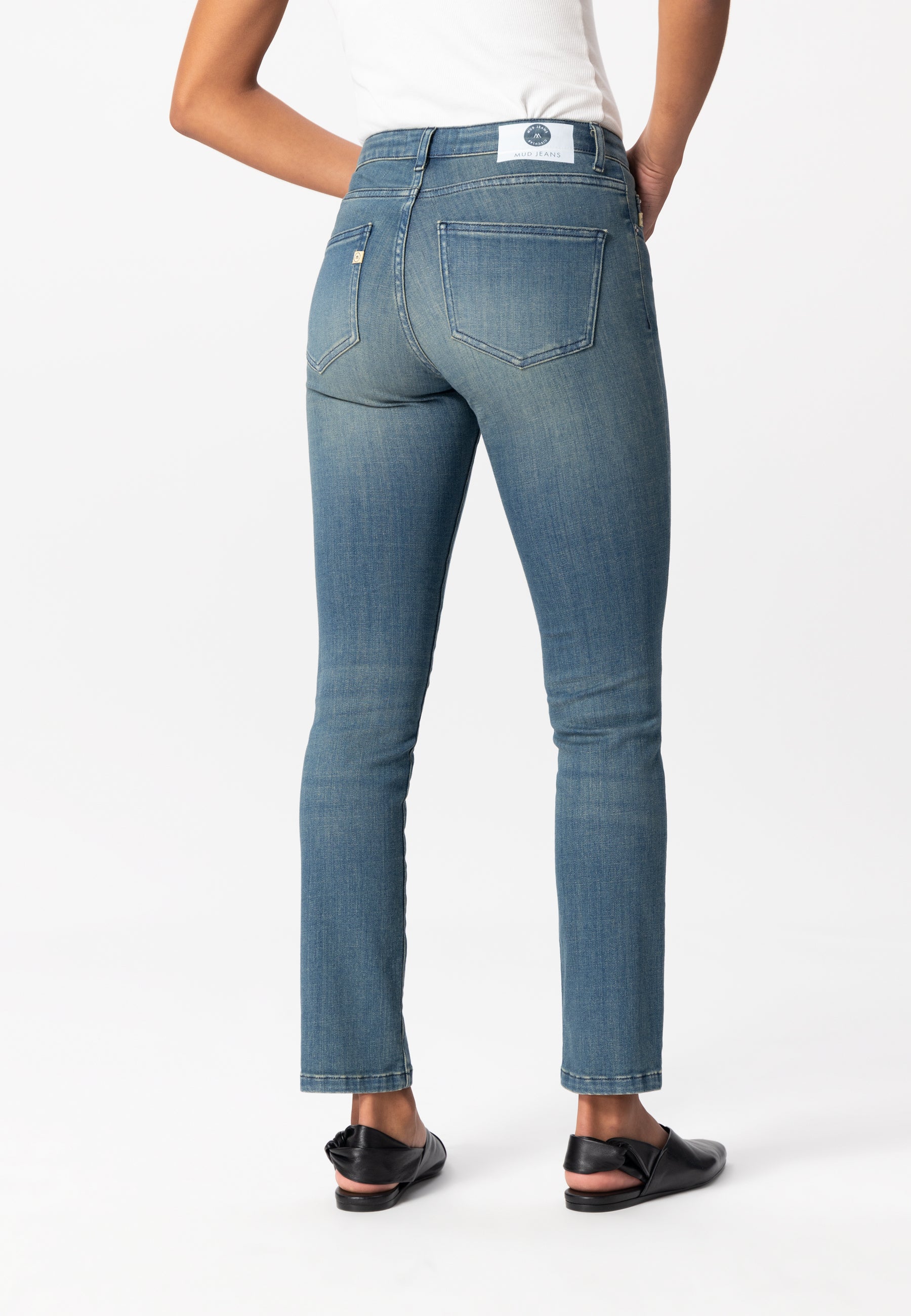 Women's sustainable blue denim jeans by MUD Jeans, slim fit, high waist, paired with black flats and a white top.